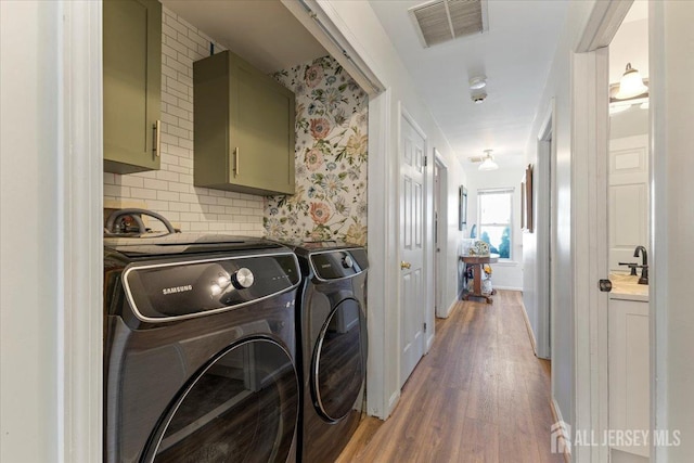 washroom with independent washer and dryer, visible vents, wood finished floors, and cabinet space
