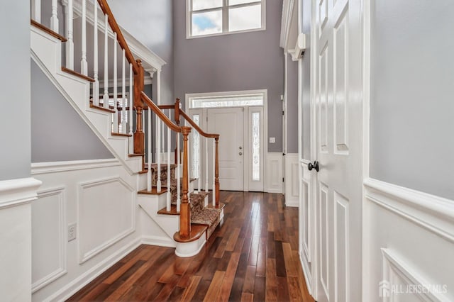 entrance foyer with a decorative wall, a wainscoted wall, dark wood-type flooring, a high ceiling, and stairway