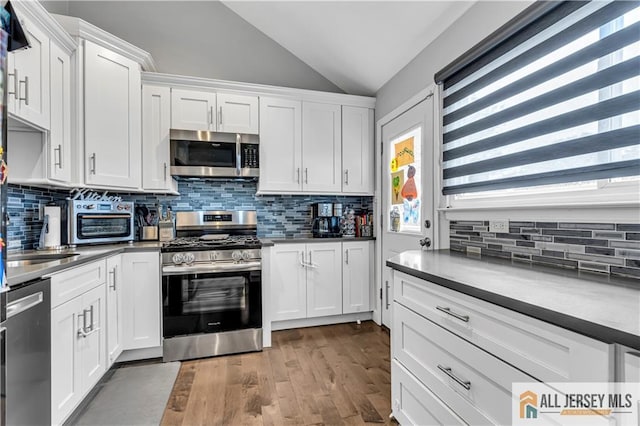 10 Buttonwood Dr, Old Bridge, NJ 08857 - kitchen with appliances with stainless steel finishes, lofted ceiling, plenty of natural light, white cabinets, and wood finished floors