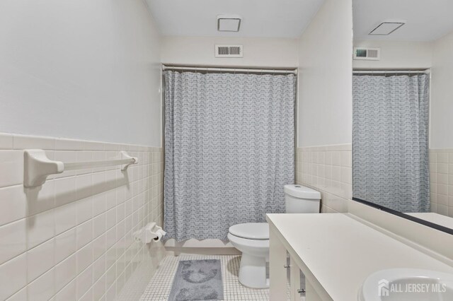 bathroom featuring tile patterned flooring, tile walls, a shower with shower curtain, vanity, and toilet