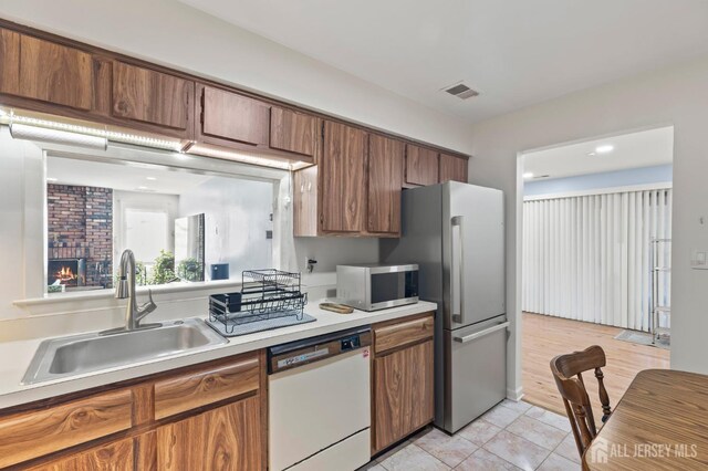 kitchen with sink, stainless steel appliances, a brick fireplace, and light tile patterned flooring