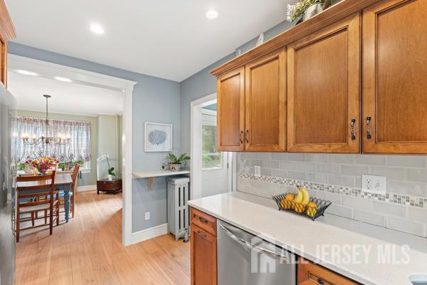 185 Rowland Pl, Woodbridge Proper, NJ 07095 - kitchen with stainless steel dishwasher, radiator heating unit, tasteful backsplash, light wood finished floors, and light countertops