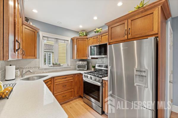 185 Rowland Pl, Woodbridge Proper, NJ 07095 - kitchen with appliances with stainless steel finishes, light countertops, decorative backsplash, light wood finished floors, and brown cabinetry