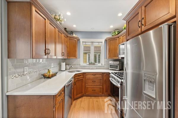 185 Rowland Pl, Woodbridge Proper, NJ 07095 - kitchen with stainless steel appliances, brown cabinetry, light wood-style flooring, tasteful backsplash, and recessed lighting