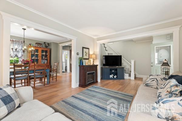 185 Rowland Pl, Woodbridge Proper, NJ 07095 - living room featuring wood finished floors, stairway, ornamental molding, a chandelier, and a glass covered fireplace