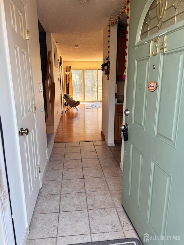 hall featuring a textured ceiling, baseboards, and light tile patterned floors