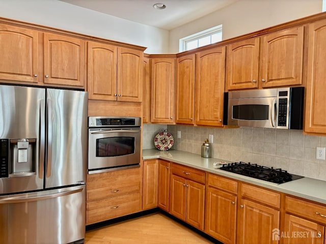 kitchen featuring light wood-style flooring, brown cabinetry, appliances with stainless steel finishes, light countertops, and backsplash