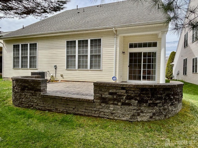 rear view of property featuring a lawn, central AC unit, a patio, and a shingled roof