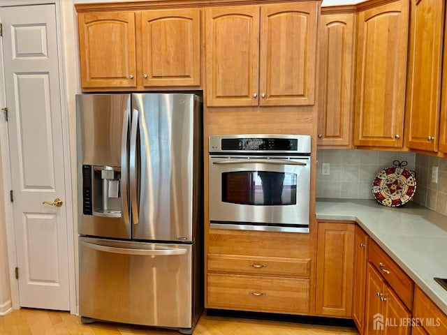 kitchen featuring stainless steel appliances, brown cabinetry, light wood-type flooring, backsplash, and light countertops
