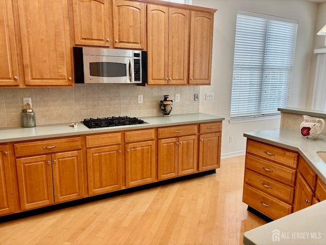 kitchen featuring light wood-style floors, decorative backsplash, black gas cooktop, and stainless steel microwave