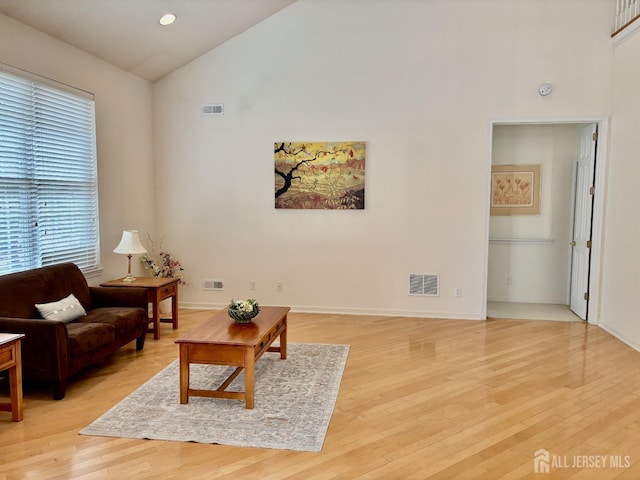 living area featuring baseboards, visible vents, light wood finished floors, and high vaulted ceiling