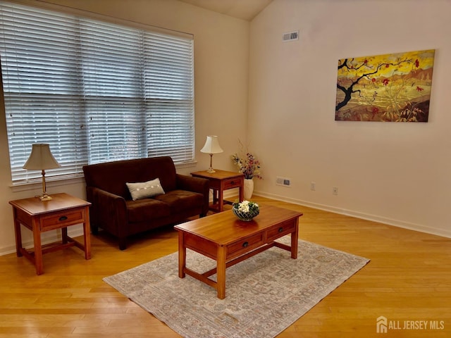 living room with visible vents, baseboards, lofted ceiling, and light wood-type flooring