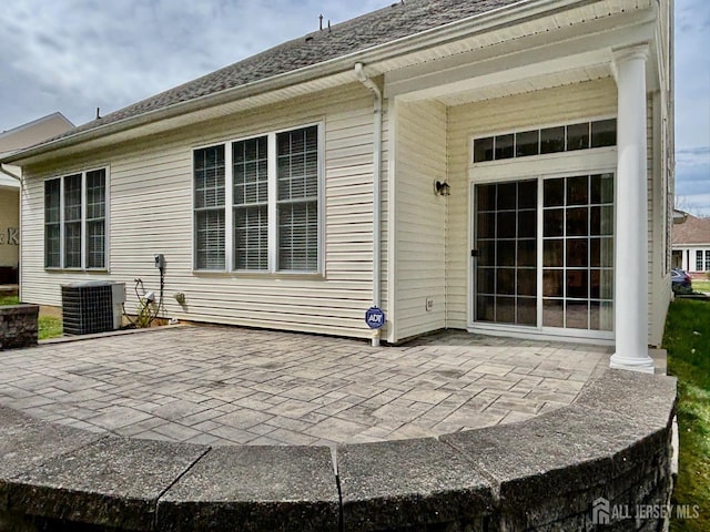 back of property featuring roof with shingles, central AC, and a patio