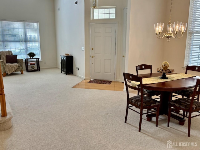 dining room with a towering ceiling, an inviting chandelier, carpet, and baseboards