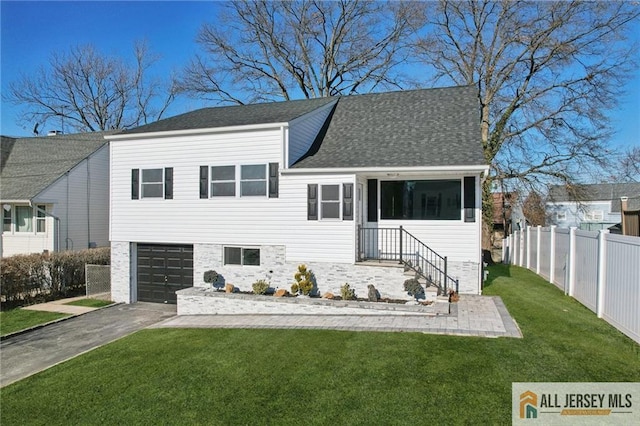 tri-level home featuring fence, driveway, a shingled roof, a front lawn, and a garage