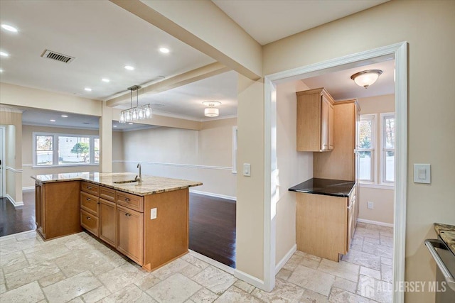 kitchen with hanging light fixtures, an island with sink, sink, and light stone counters