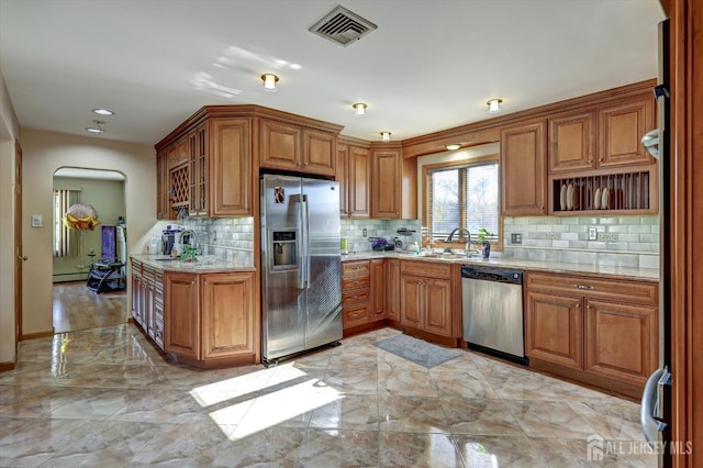 kitchen featuring a baseboard heating unit, sink, light stone countertops, appliances with stainless steel finishes, and tasteful backsplash