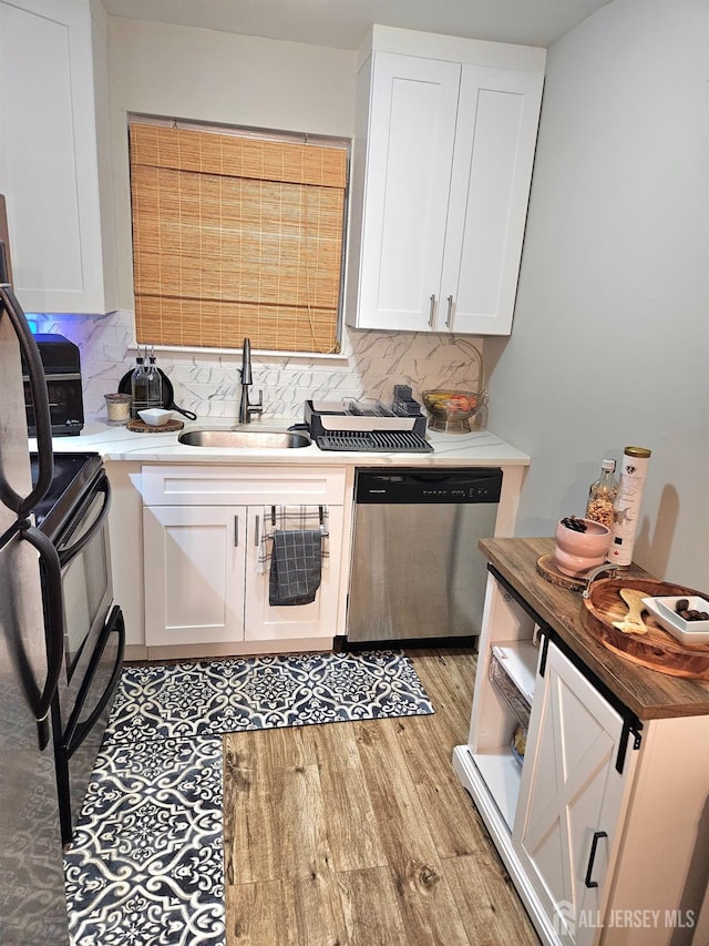 kitchen featuring white cabinets, backsplash, stainless steel dishwasher, a sink, and light wood-type flooring