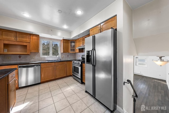 kitchen featuring appliances with stainless steel finishes, dark countertops, brown cabinetry, a sink, and backsplash