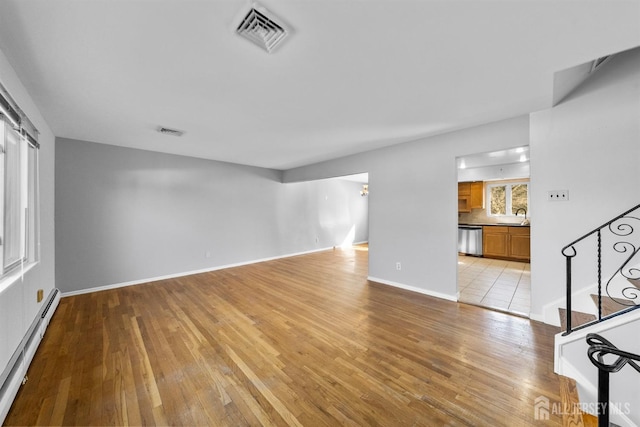 unfurnished living room featuring a baseboard heating unit, light wood finished floors, a sink, and baseboards
