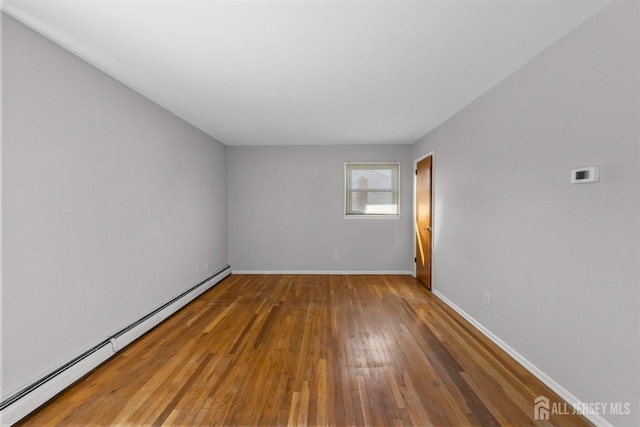 spare room featuring baseboard heating, wood-type flooring, and baseboards