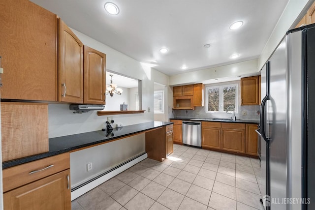 kitchen with appliances with stainless steel finishes, a baseboard heating unit, a sink, light tile patterned floors, and dark countertops