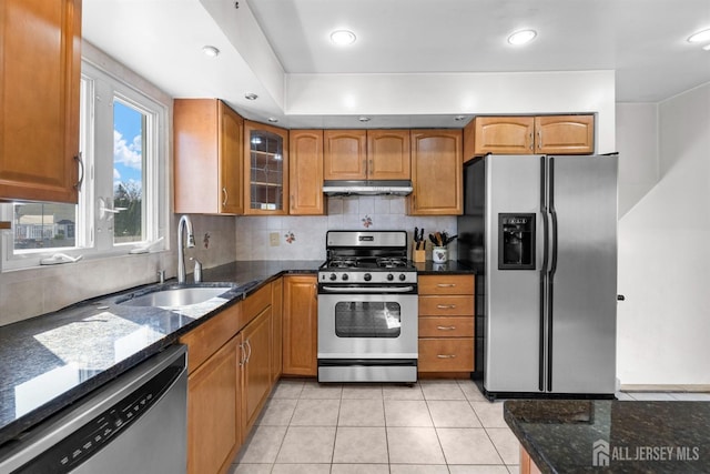 kitchen featuring stainless steel appliances, a sink, dark stone counters, brown cabinetry, and recessed lighting