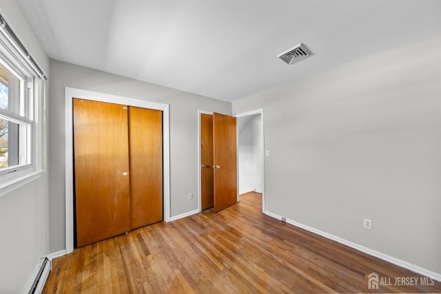 unfurnished bedroom with a baseboard heating unit, wood finished floors, baseboards, and a closet