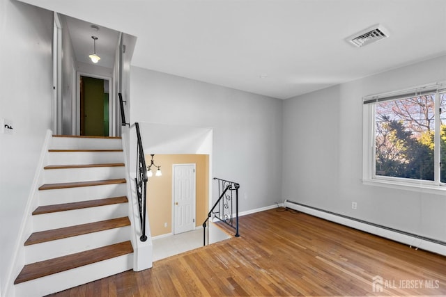 staircase with a baseboard heating unit, wood finished floors, and baseboards