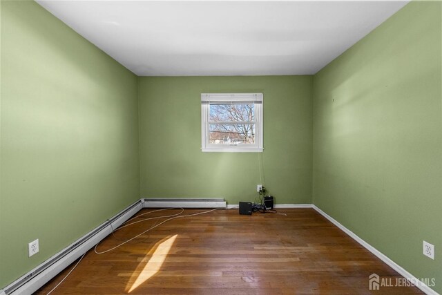 empty room featuring baseboards, wood finished floors, and a baseboard radiator