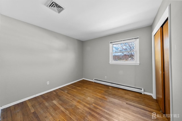unfurnished bedroom with baseboard heating, wood finished floors, baseboards, and a closet