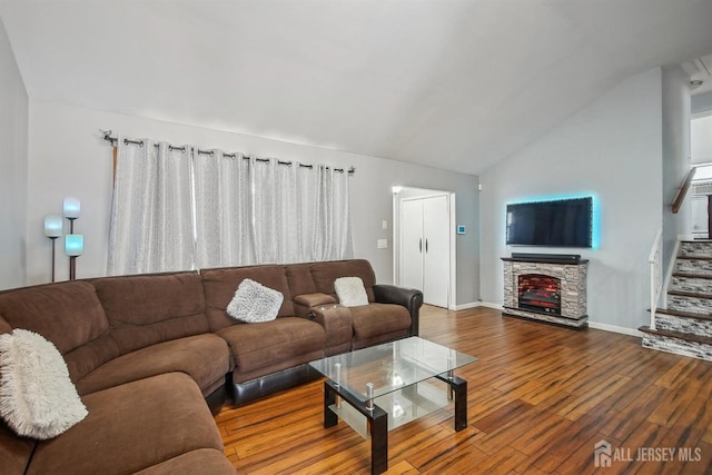 living room with a fireplace, lofted ceiling, wood finished floors, baseboards, and stairs