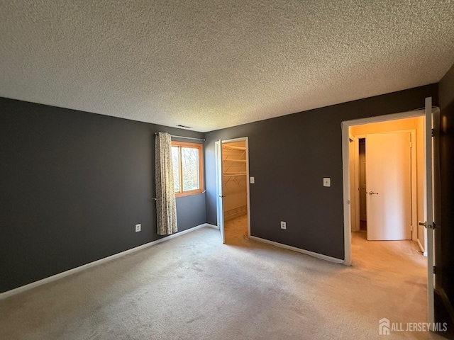 unfurnished bedroom with light carpet, baseboards, a walk in closet, and a textured ceiling