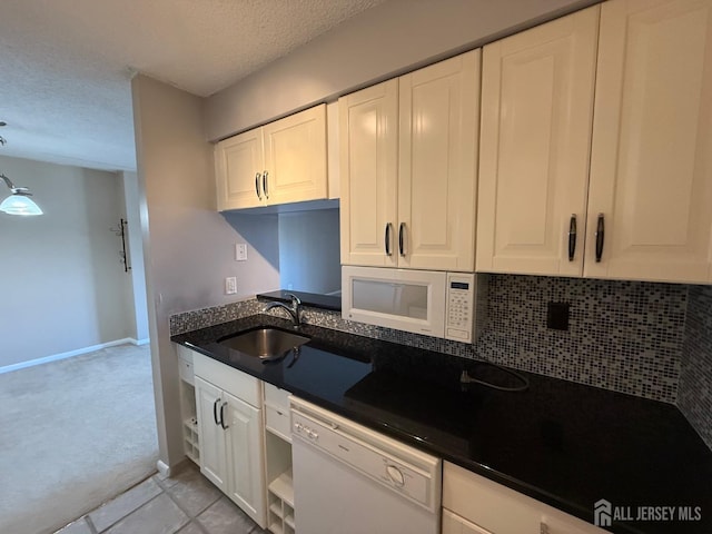 kitchen featuring light tile patterned floors, tasteful backsplash, white cabinets, a sink, and white appliances