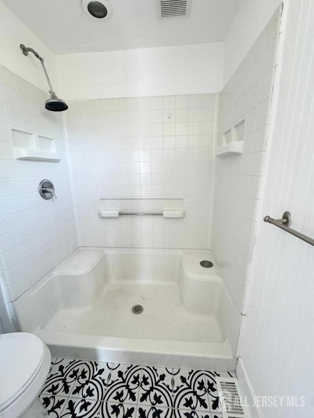 bathroom featuring tiled shower, tile patterned flooring, and toilet