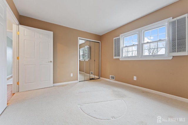 unfurnished bedroom with baseboards, visible vents, light colored carpet, and a closet