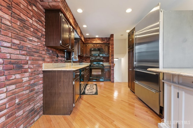 kitchen with brick wall, dark brown cabinets, black appliances, light wood-type flooring, and light stone counters