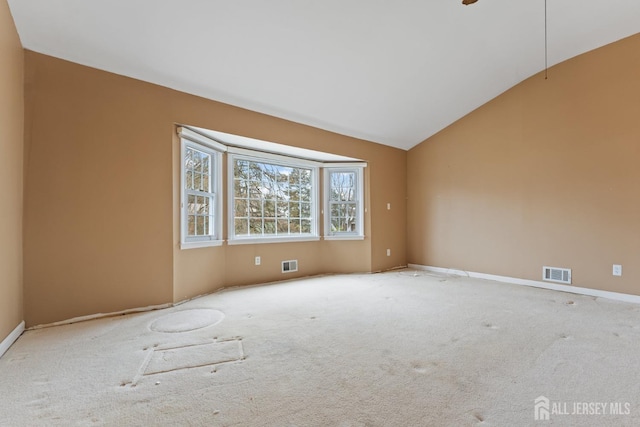 carpeted spare room with baseboards, visible vents, and vaulted ceiling