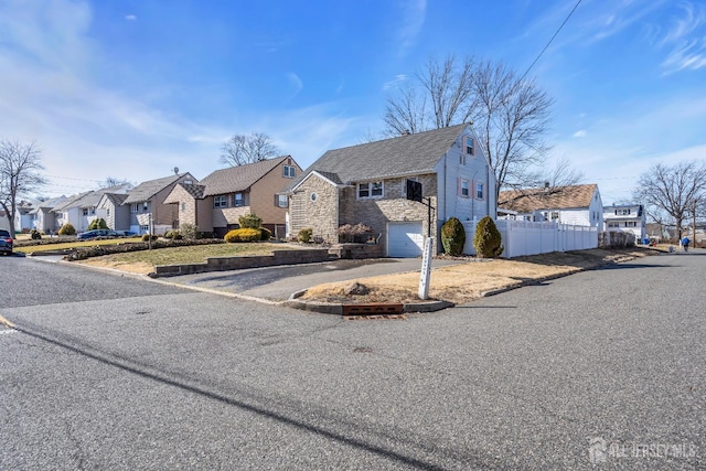 view of front of property featuring driveway, a residential view, fence, an attached garage, and stone siding