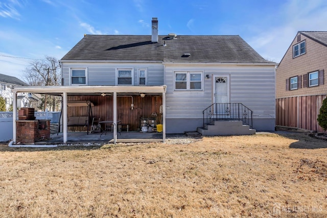 back of house with a chimney, a patio area, fence, a yard, and a shingled roof