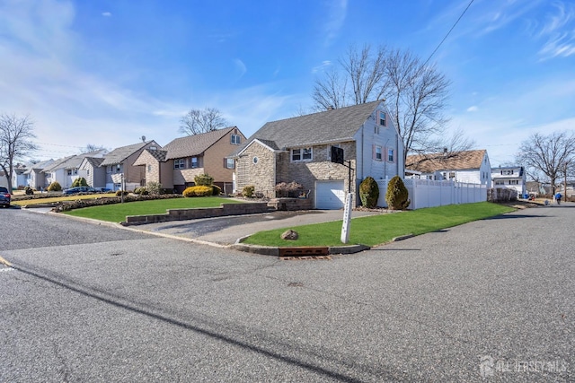 traditional-style home with a residential view, fence, an attached garage, a front lawn, and driveway