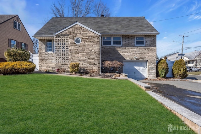 view of front of house featuring a front yard, stone siding, roof with shingles, an attached garage, and driveway