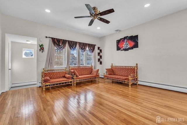 living area featuring wood-type flooring, a ceiling fan, plenty of natural light, and baseboard heating