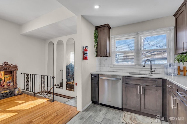 kitchen with dark brown cabinetry, light wood-type flooring, light countertops, a sink, and dishwasher