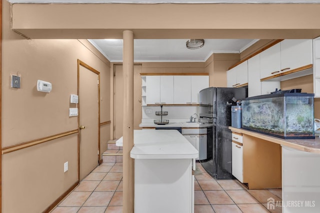 kitchen featuring crown molding, freestanding refrigerator, light tile patterned flooring, light countertops, and white cabinetry