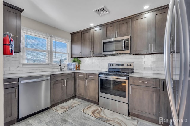 kitchen with dark brown cabinetry, visible vents, appliances with stainless steel finishes, a sink, and light countertops