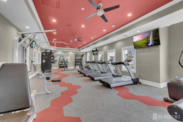 gym with a tray ceiling, light colored carpet, and ceiling fan