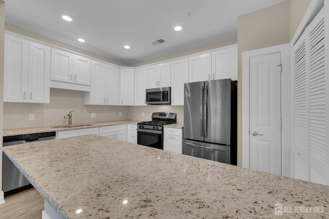 kitchen featuring white cabinetry, appliances with stainless steel finishes, light stone countertops, and sink