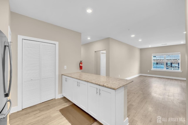 kitchen with stainless steel refrigerator, white cabinets, light stone counters, kitchen peninsula, and light hardwood / wood-style floors