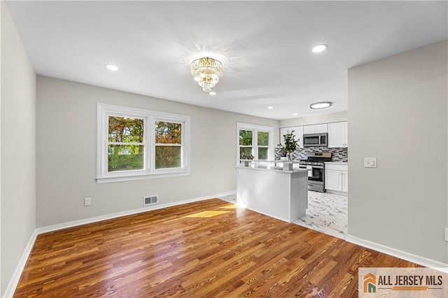 empty room featuring white cabinetry, an inviting chandelier, light wood-type flooring, and kitchen peninsula